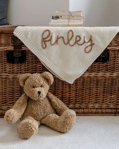 a teddy bear sitting in front of a basket with a personalized handkerchief on it