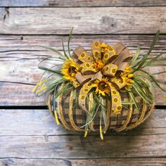 a plaid pumpkin with yellow flowers in it sitting on a wooden table next to wood planks