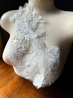 a mannequin with white lace and beads on it's neck, sitting on top of a wooden table