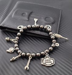 These cute and classy custom Beaded Car Part Charm Bracelets are trendy and will surely make a statement! Create a unique bracelet that shows off your unique style! This bracelet can fit up to 15 charms. Charm Options: - Option#1: Fully Custom Bracelet (Plain Bracelet/ No Charms) Please order your charms for this option here: Charm Listing - Option#2: 15 Random Charms - Option#3: Driver’s Bracelet Turbo, Car Keys & Remote, Steering Wheel, Gear, Stoplight, Wrench, Mini Racecar - Option#4: Mechanic’s Special Wrench, Crescent Wrench, Hex Nut, Spark Plug, Heart Gear, Piston, Screwdriver - Option#5: Track Edition Racing Seat, Turbo, Racing Flag, Wheel / Tire, Mini Racecar, Stoplight, Wrench - Option#6: Rotary Lover Rotary, Steering Wheel, Car Keys & Remote, Mini Racecar, Gear, Wrench, Hex Nut T Trendy Metal Wristband As Gift, Magnetic Metal Bracelet Jewelry, Nickel Free Novelty Bracelet Jewelry, Adjustable Magnetic Metal Bracelet, Novelty Charms Bracelet Jewelry, Novelty Jewelry Charms Bracelet, Metal Stretch Bracelet With Round Beads For Gift, Adjustable Black Bracelets With Charms, Black Novelty Bracelet Jewelry