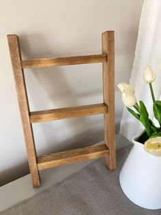 a wooden shelf next to a vase with flowers in it and a white curtain behind it