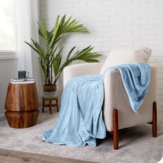 a chair with a blanket on it next to a potted plant in a living room