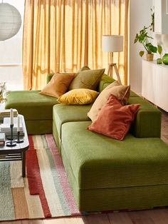 a living room with green couches and colorful pillows on the sofa, in front of a yellow curtained window