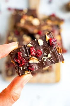 someone holding up a piece of chocolate with nuts and cranberries