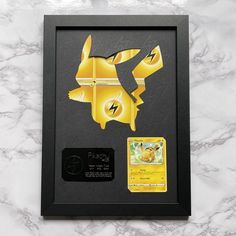 a yellow pokemon pikachu paper cutout in a black frame on a marble surface