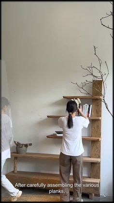 a woman standing in front of a book shelf next to a tree with no leaves