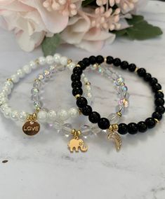 "Beautiful stretch bead bracelets with gold charms and 6mm white marble, crystal or black onyx beads, as well as gold spacers. This listing is for one bracelet with one charm. If you're looking for another color, send me a message! The bracelets shown are approximately 7\" in length. The charm options shown are gold 18k gold plated moon with cubic zirconia charms, light gold elephant and light gold alloy flat round with \"love\"." Beads Charm Bracelet, Charm Beads Bracelet, White And Black Bracelet, Beads Bracelet With Charms, Crystal Beaded Bracelets Diy, Black Crystal Bracelet, Cute Charm Bracelet, Beaded Bracelets Crystal, Handmade Bracelets With Beads