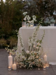 white flowers and candles sit on the ground next to a table with a white cloth