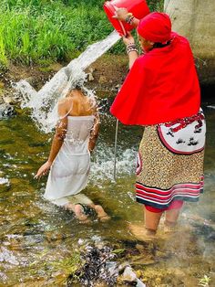 two women are standing in the water, one is holding a red bucket and the other is wearing a white dress