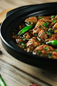 a black bowl filled with food on top of a wooden table next to green beans