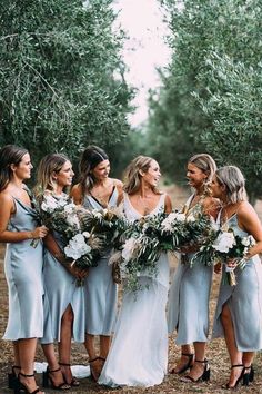 a group of women standing next to each other in front of an olive tree filled field