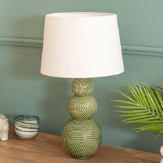 a green lamp sitting on top of a wooden table next to a potted plant