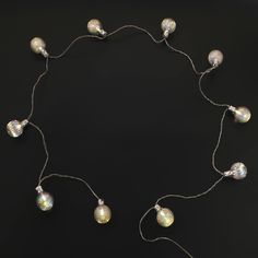 a necklace with white glass beads and silver wire on a black background, in the shape of a circle