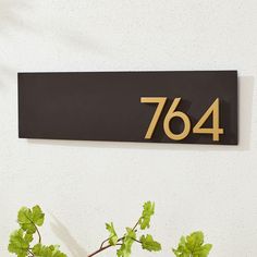 a house number sign mounted to the side of a white wall next to a potted plant