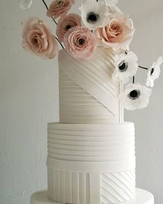 a three tiered white cake with pink and white flowers on the top, along with black and white stripes