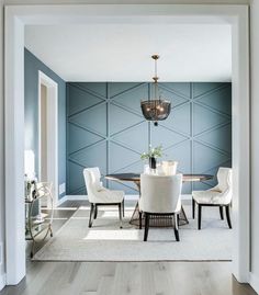 a dining room with blue walls, white chairs and a chandelier hanging from the ceiling