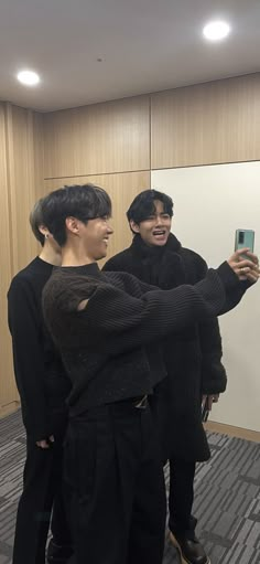 two young men standing in front of a mirror taking a selfie with their cell phone