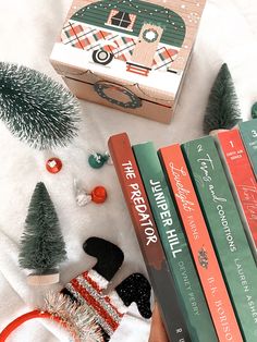 a person holding three books in their hands next to christmas decorations and other items on a white blanket