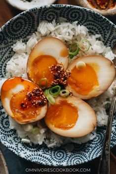 three hard boiled eggs on top of rice in a blue and white bowl