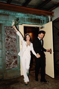 a man and woman are holding hands as they walk into an open door with flowers in their hand