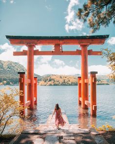 a woman standing in front of a large body of water under a red torido