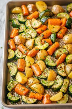 roasted vegetables in a baking pan with herbs on top, including carrots and zucchini