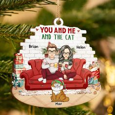 a christmas ornament with a couple sitting on a couch next to a cat