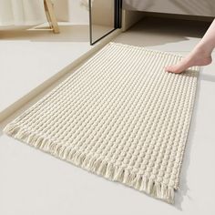 a person standing on the floor next to a bed with a white blanket and rug