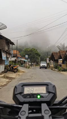 a motorcycle is driving down the road in front of some houses on a foggy day