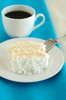 a piece of cake sitting on top of a white plate next to a cup of coffee