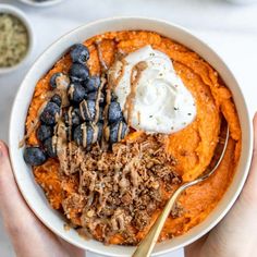 two hands holding a bowl of sweet potato breakfast bowls with whipped cream and blueberries