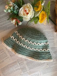 a crocheted hat sitting on top of an open book next to some flowers