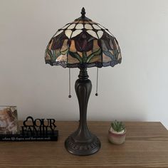 a lamp sitting on top of a wooden table next to a potted plant and a book