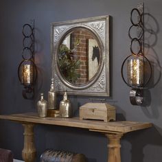 a wooden table sitting under a mirror next to a wall mounted light fixture with lights on it