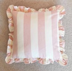 a pink and white striped pillow with ruffles on the bottom, sitting on carpet