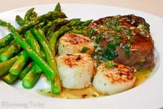 scallops and asparagus are served on a white plate with brown gravy