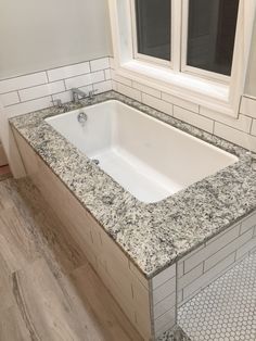 a bath tub sitting next to a window on top of a tiled floor in a bathroom