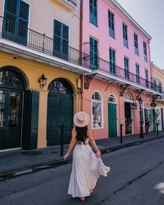 a woman in a white dress and hat walking down the street next to colorful buildings