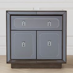 a grey cabinet with two doors and one drawer on the bottom, in front of a white wall