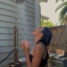 a woman standing in front of a house drinking out of a water faucet