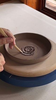 a person using a pencil to draw on a clay plate with a flower design in the center