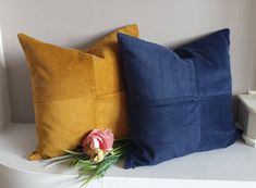 two blue and yellow pillows sitting on top of a white shelf next to each other