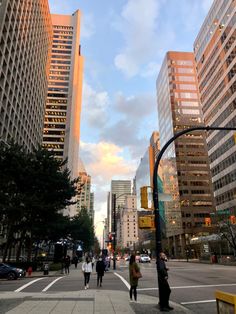 people are walking on the sidewalk in front of tall buildings and traffic lights at dusk