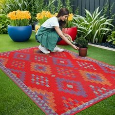 a woman kneeling down to plant a potted plant on top of a red rug