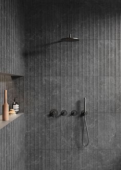 a bathroom with grey tile and black fixtures on the wall, along with a shower head