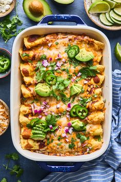 an enchilada casserole in a blue dish surrounded by sliced avocados