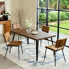 a dining room table with four chairs and a rug in front of the window that overlooks a garden