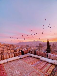 many balloons are flying in the sky above an area that is covered with colorful rugs