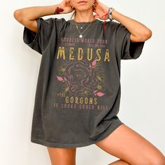 Get ready to be OBSESSED with your new Medusa shirt. It's the cutest and most trendy way to combine all those important trendy Greek Mythology, feminism and light academia vibes! This is the perfect snake shirt!  * Q U I C K * F A C T S * ✺  All shirts are UNISEX ✺  100%  ringspun cotton (fiber content may vary for different colors) ✺  Soft-washed, garment-dyed fabric brings extra coziness ✺  Wash and dry normally (on cool for best results) ✺  Sewn-in twill label * S I Z I N G * ✺ For an oversized fit, select two or three sizes up from your normal size ✺ Model is wearing size L  ✺ Sizing runs true to size ✺ Relaxed fit ✺ Most women find their typical size works best, since they are meant to fit a touch loose ✺ See Size guide and fit in images          * S H I P P I N G * T I M E S * ✺ Our Fairy Grunge Cotton Tops With Letter Print, Cotton Short Sleeve Goblincore T-shirt, Fairy Grunge Cotton Tops With Crew Neck, Fairy Grunge Short Sleeve Top With Relaxed Fit, Fairy Grunge Relaxed Fit Short Sleeve Tops, Goblincore Cotton Crew Neck Top, Goblincore Short Sleeve T-shirt For Summer, Summer Goblincore T-shirt With Short Sleeves, Summer Goblincore Short Sleeve T-shirt