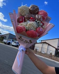 a person is holding a bouquet of cookies and candies in the street with cars parked behind them